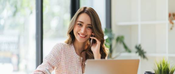 Junge Frau am Schreibtisch hält ein Telefon ans Ohr
